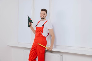 Photo of Worker holding tools for installation roller window blinds indoors