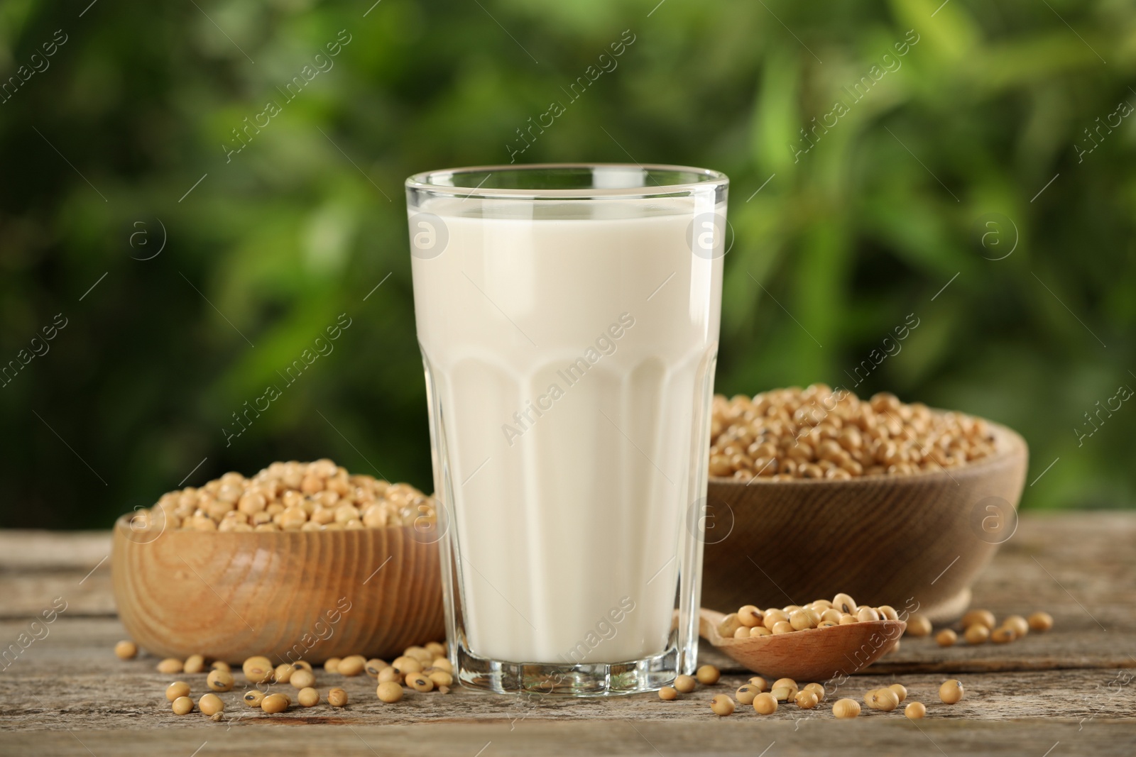 Photo of Glass with fresh soy milk and grains on white wooden table against blurred background