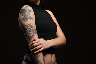 Woman with tattoos on arm against black background, closeup