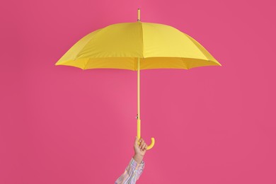 Photo of Woman with open yellow umbrella on pink background, closeup
