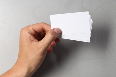 Photo of Man holding white blank cards at light grey table, top view. Mockup for design