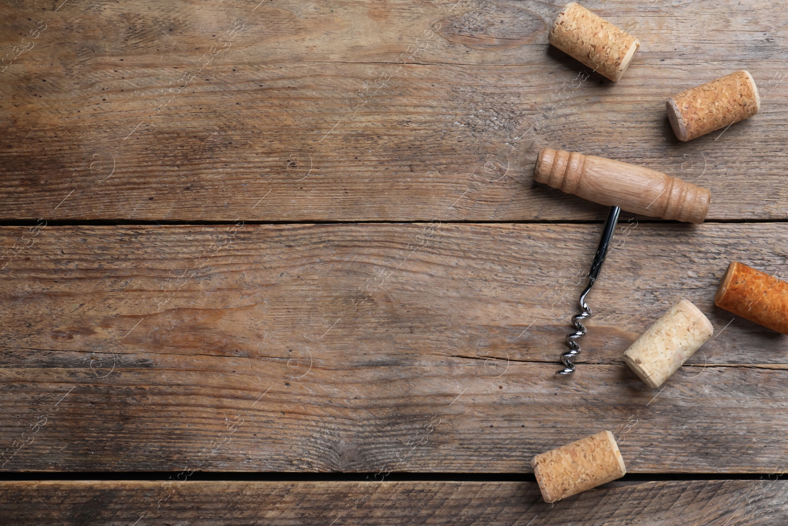Photo of Corkscrew and wine corks on wooden table, flat lay. Space for text