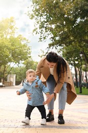 Mother supporting her little son while he learning to walk outdoors