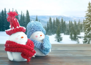 Image of Cute decorative snowmen on wooden table in mountains, space for text