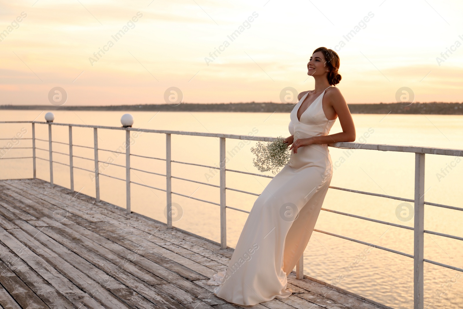 Photo of Gorgeous bride in beautiful wedding dress with bouquet near river on sunset. Space for text