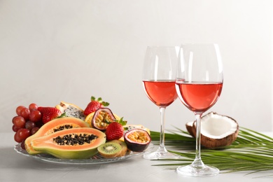 Delicious exotic fruits and glasses of wine on light grey table