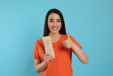 Photo of Happy young woman with tasty shawarma showing thumb up on turquoise background