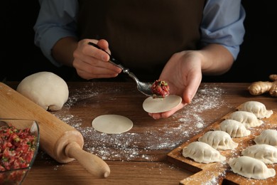 Photo of Woman putting gyoza filling in center of dough wrapper at wooden table, closeup