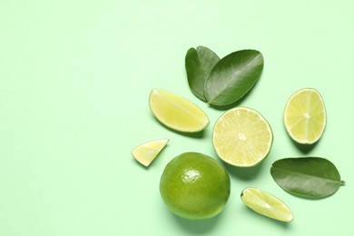 Photo of Whole and cut fresh ripe limes with leaves on light green background, flat lay