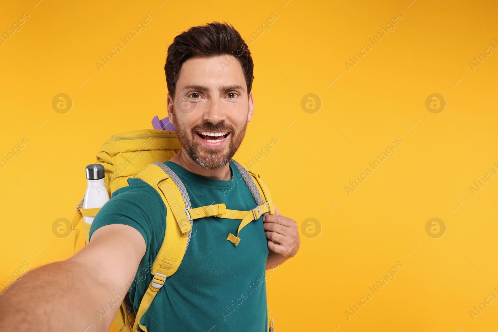 Photo of Happy man with backpack taking selfie on orange background, space for text. Active tourism