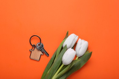 Beautiful spring flowers and key with trinket in shape of house on orange background, flat lay