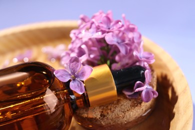 Photo of Bottle with essential oil, lilac flowers and water in bowl on violet background, closeup