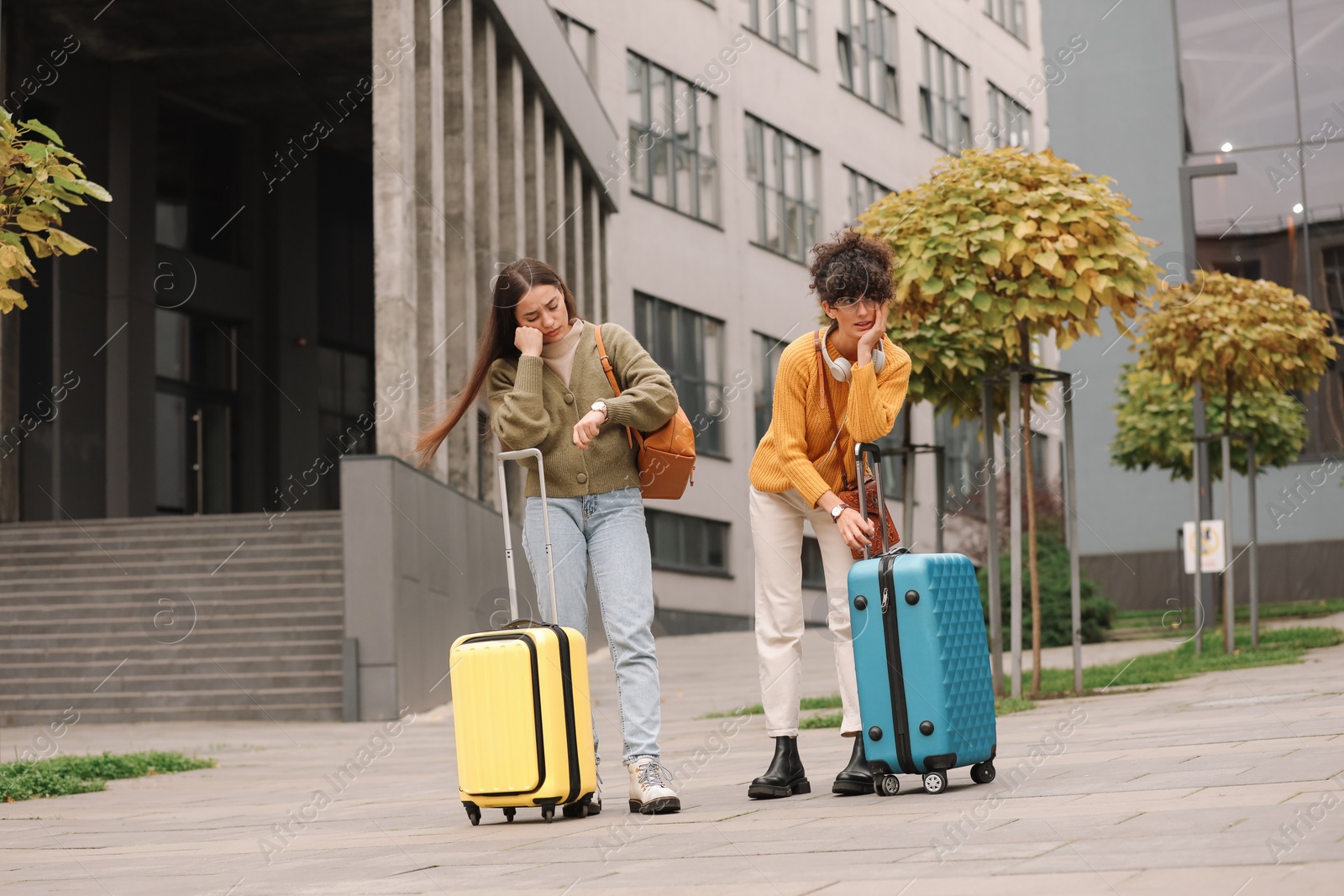 Photo of Being late. Worried women with suitcases near building outdoors