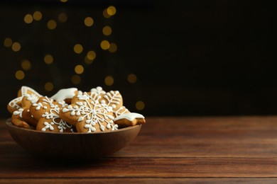 Tasty Christmas cookies with icing in bowl on wooden table against blurred lights. Space for text