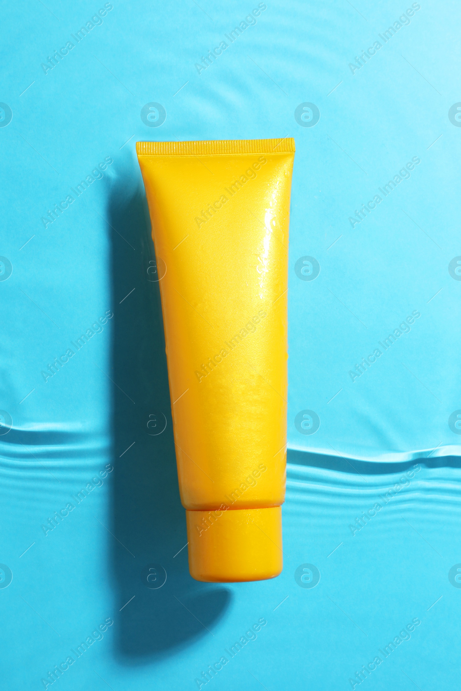 Photo of Tube with moisturizing cream in water on light blue background, top view