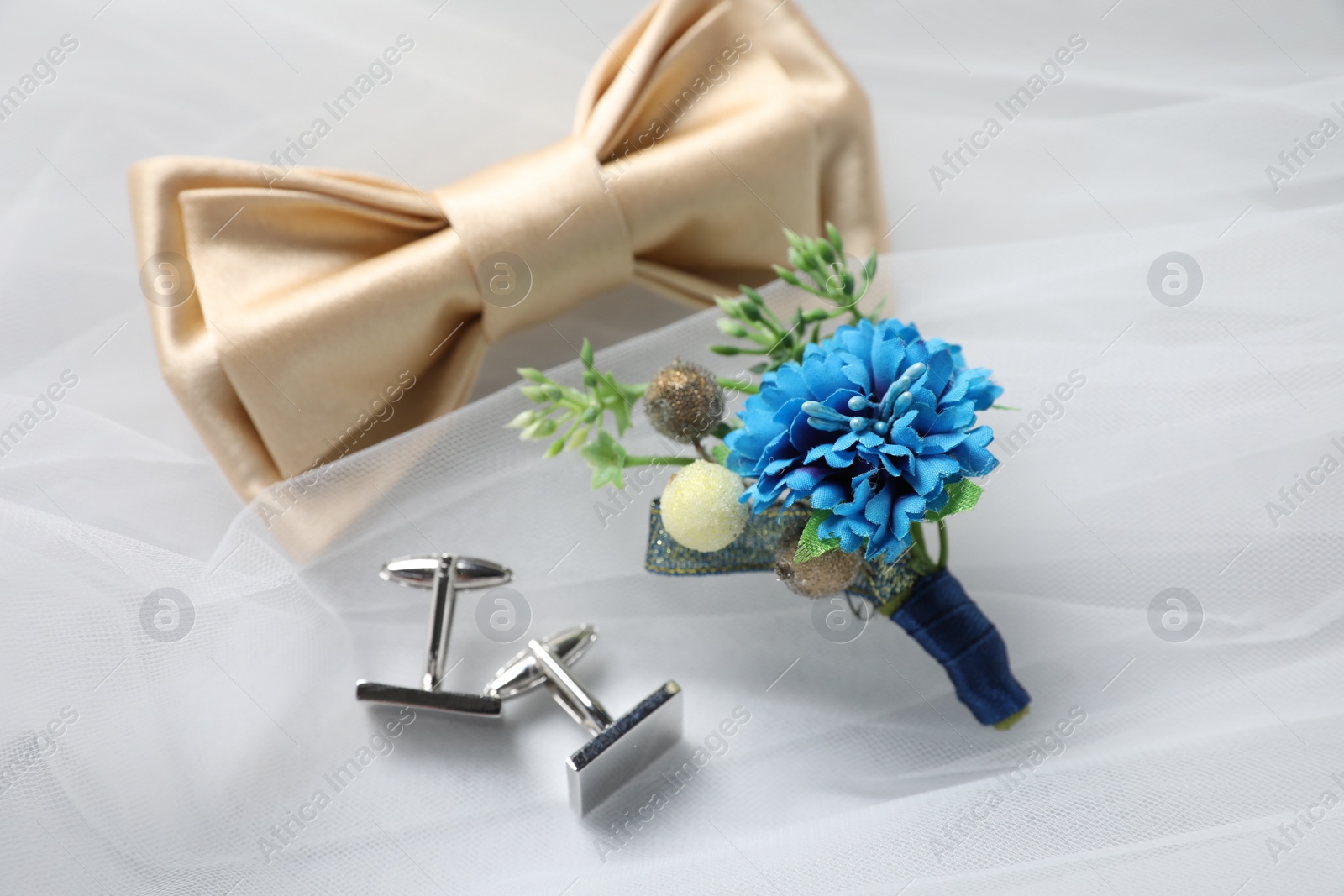 Photo of Wedding stuff. Stylish boutonniere, bow tie and cufflinks on white veil, closeup