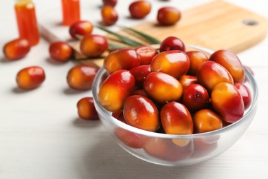 Image of Palm oil fruits in bowl on white wooden table, closeup