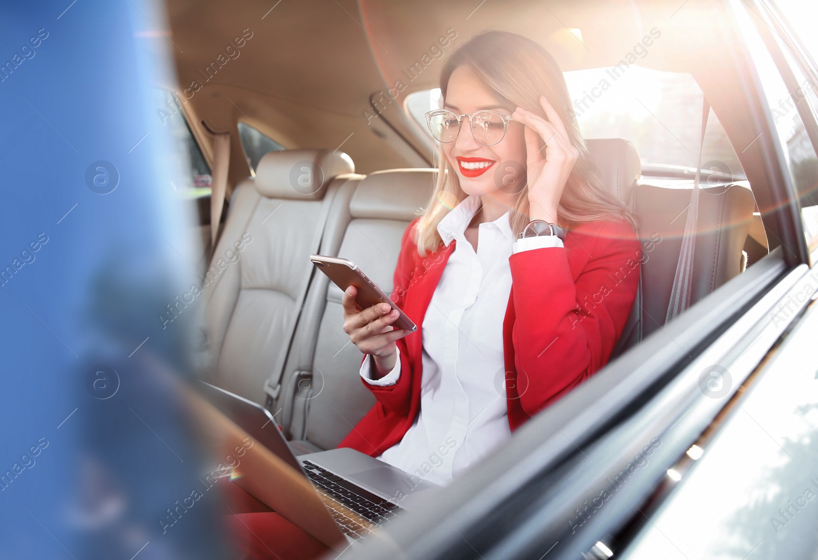 Photo of Young businesswoman with smartphone and laptop in car