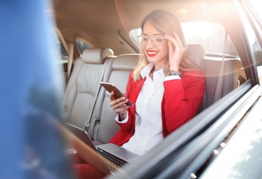 Photo of Young businesswoman with smartphone and laptop in car