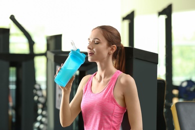 Athletic young woman drinking protein shake in gym