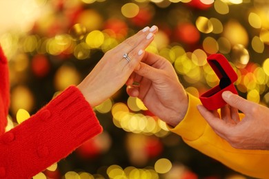 Making proposal. Man putting engagement ring on his girlfriend's finger against blurred lights, closeup