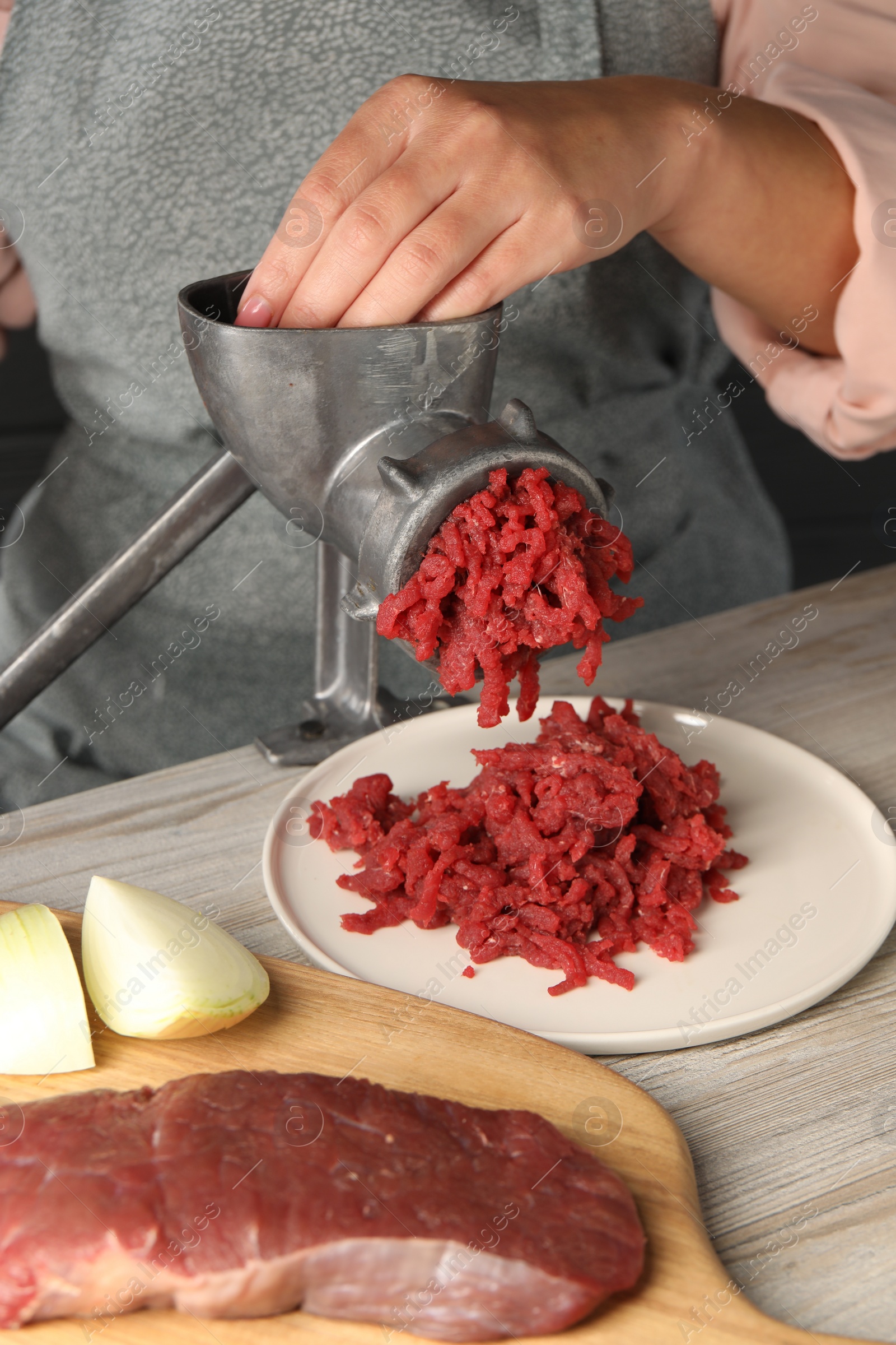 Photo of Woman making beef mince with manual meat grinder at light wooden table, closeup