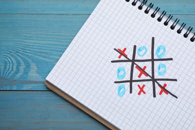 Photo of Notebook with tic tac toe game on light blue wooden table, top view