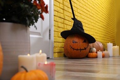 Pumpkin with drawn creepy face and burning candles near yellow brick wall in hallway. Halloween decor
