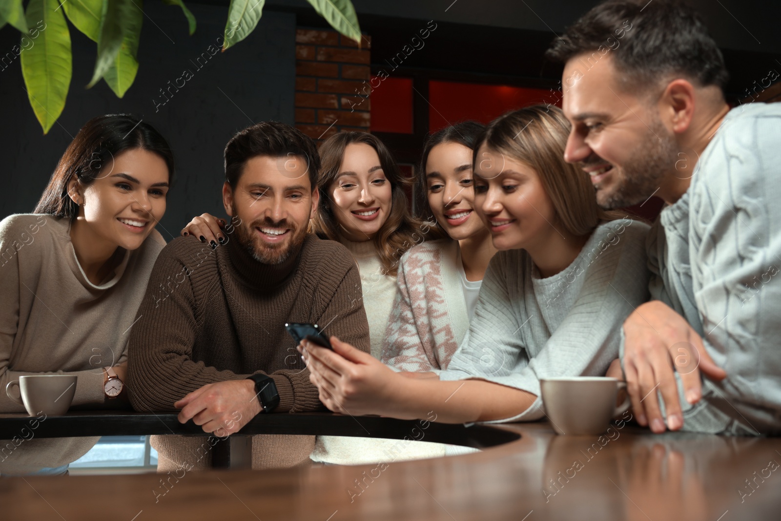 Photo of Young woman showing something funny at smartphone to her friends in cafe