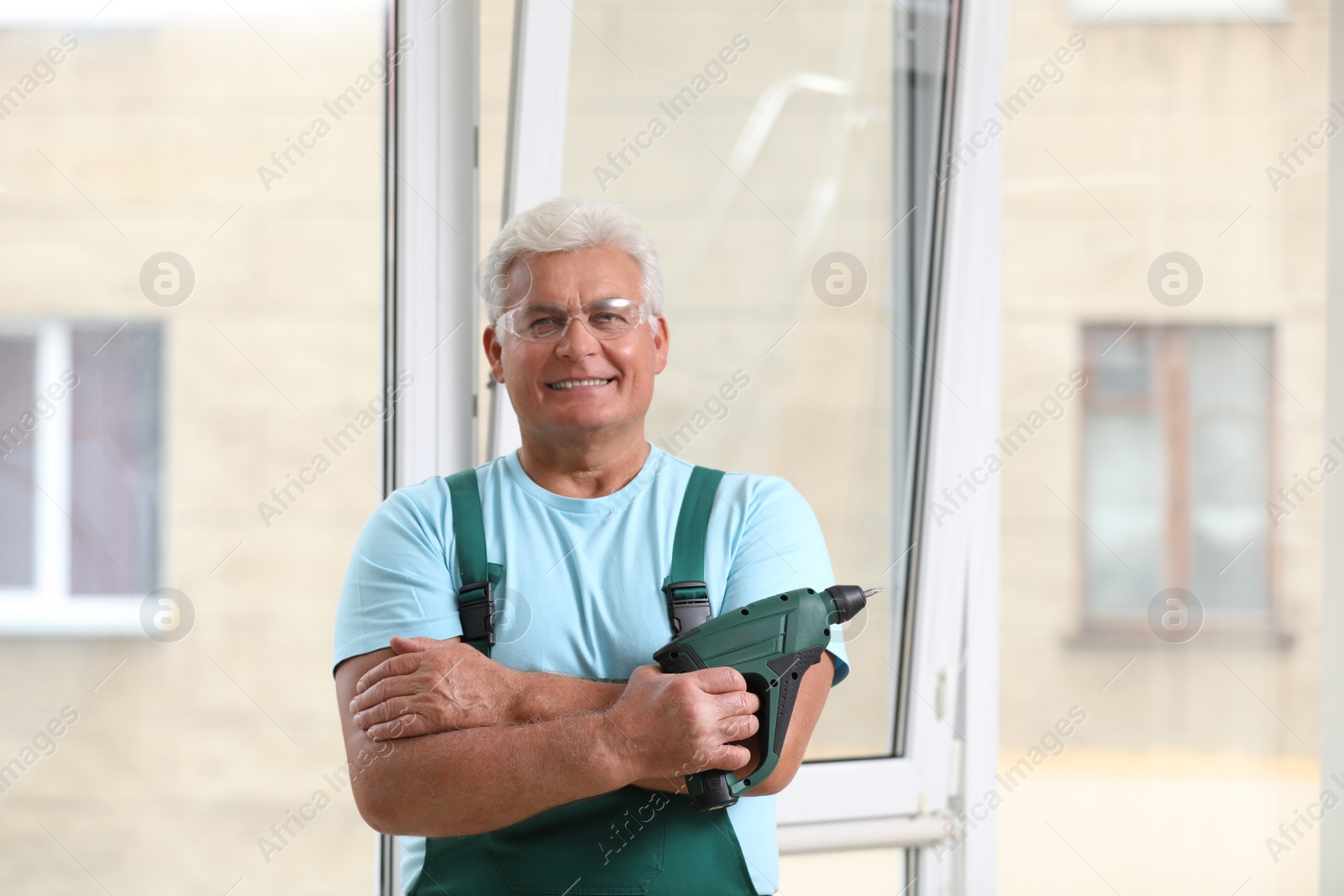 Photo of Mature repairman with electric screwdriver near plastic window indoors