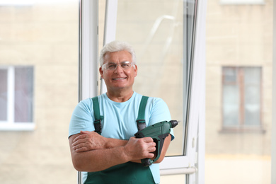 Photo of Mature repairman with electric screwdriver near plastic window indoors