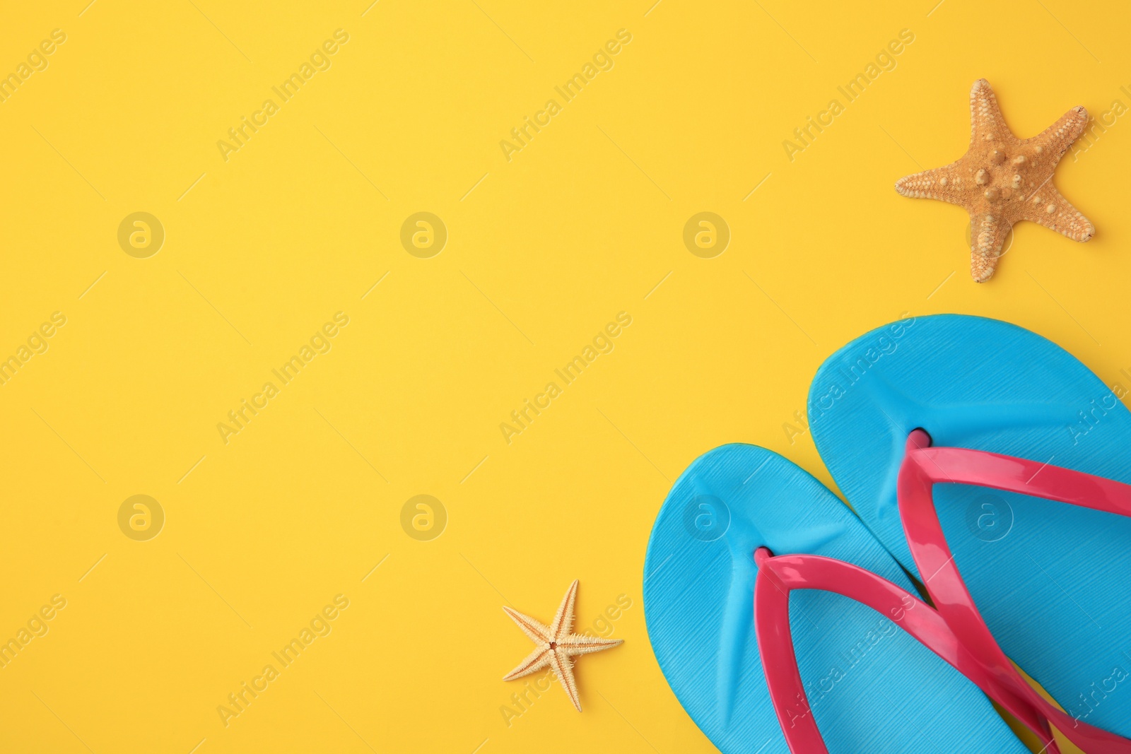 Photo of Stylish flip flops and starfishes on yellow background, flat lay with space for text