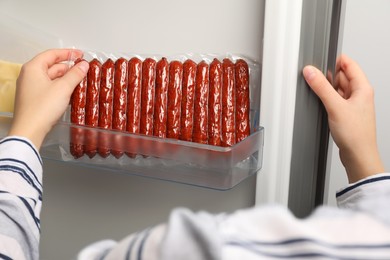 Woman putting vacuum bag with sausages into fridge, closeup. Food storage