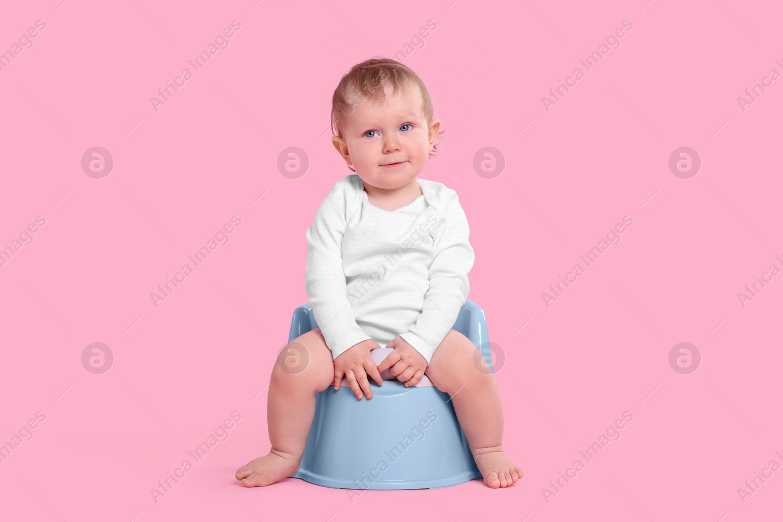 Photo of Little child sitting on baby potty against pink background