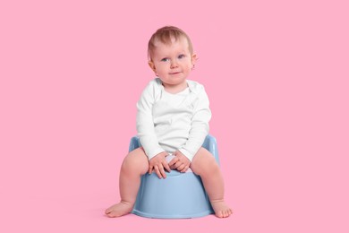 Little child sitting on baby potty against pink background