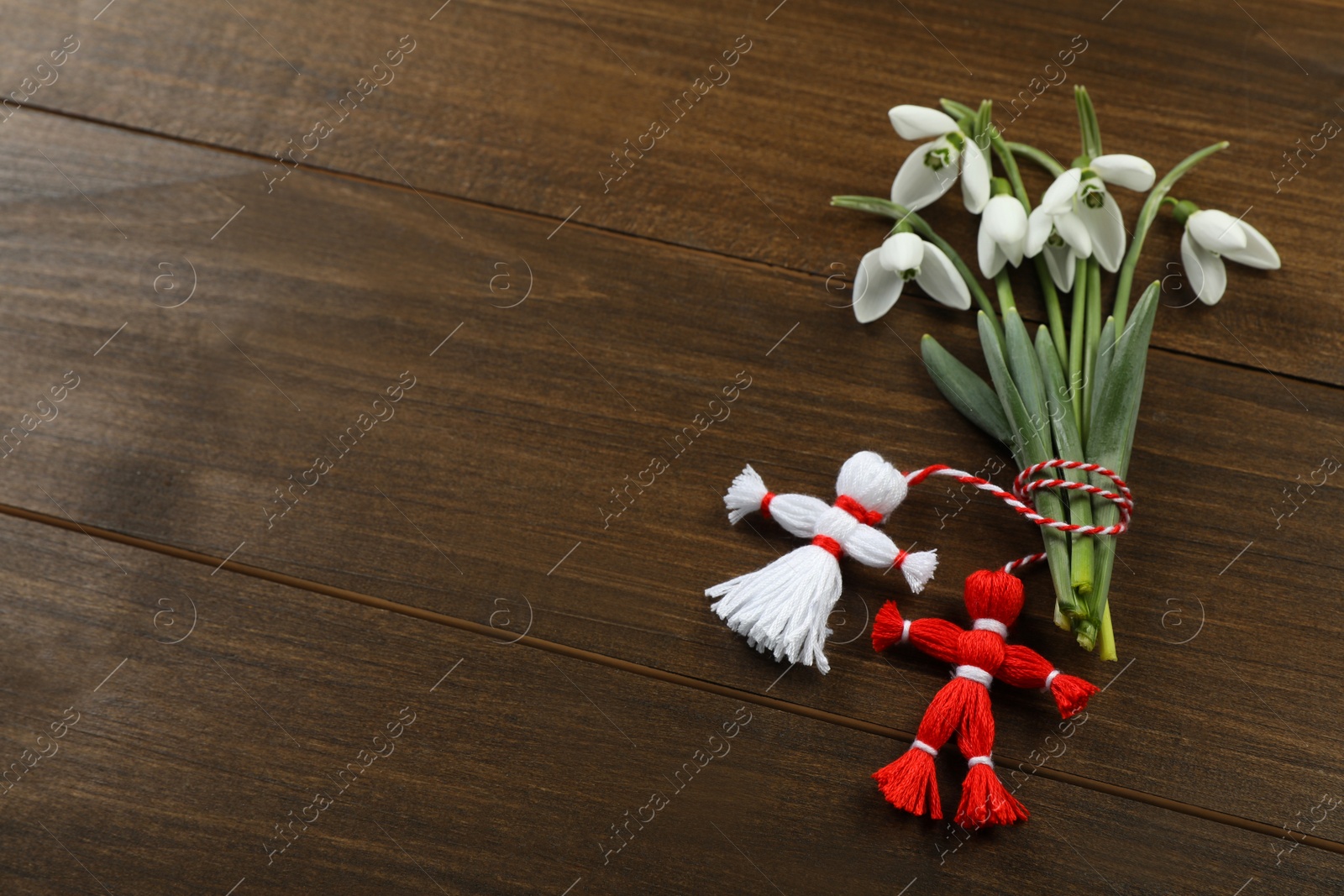 Photo of Beautiful snowdrops with traditional martisor on wooden table, flat lay and space for text. Symbol of first spring day