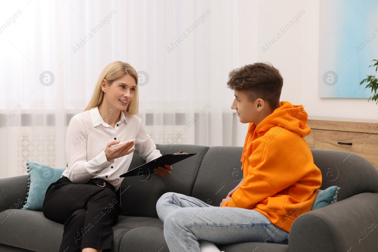 Photo of Psychologist working with teenage boy on sofa in office