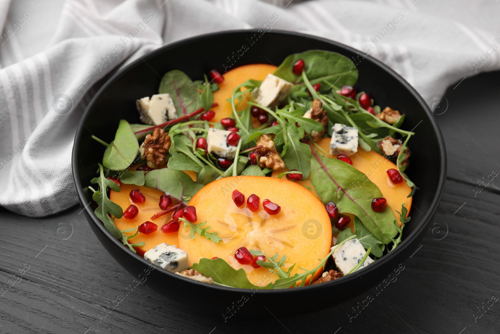 Photo of Tasty salad with persimmon, blue cheese, pomegranate and walnuts served on wooden table