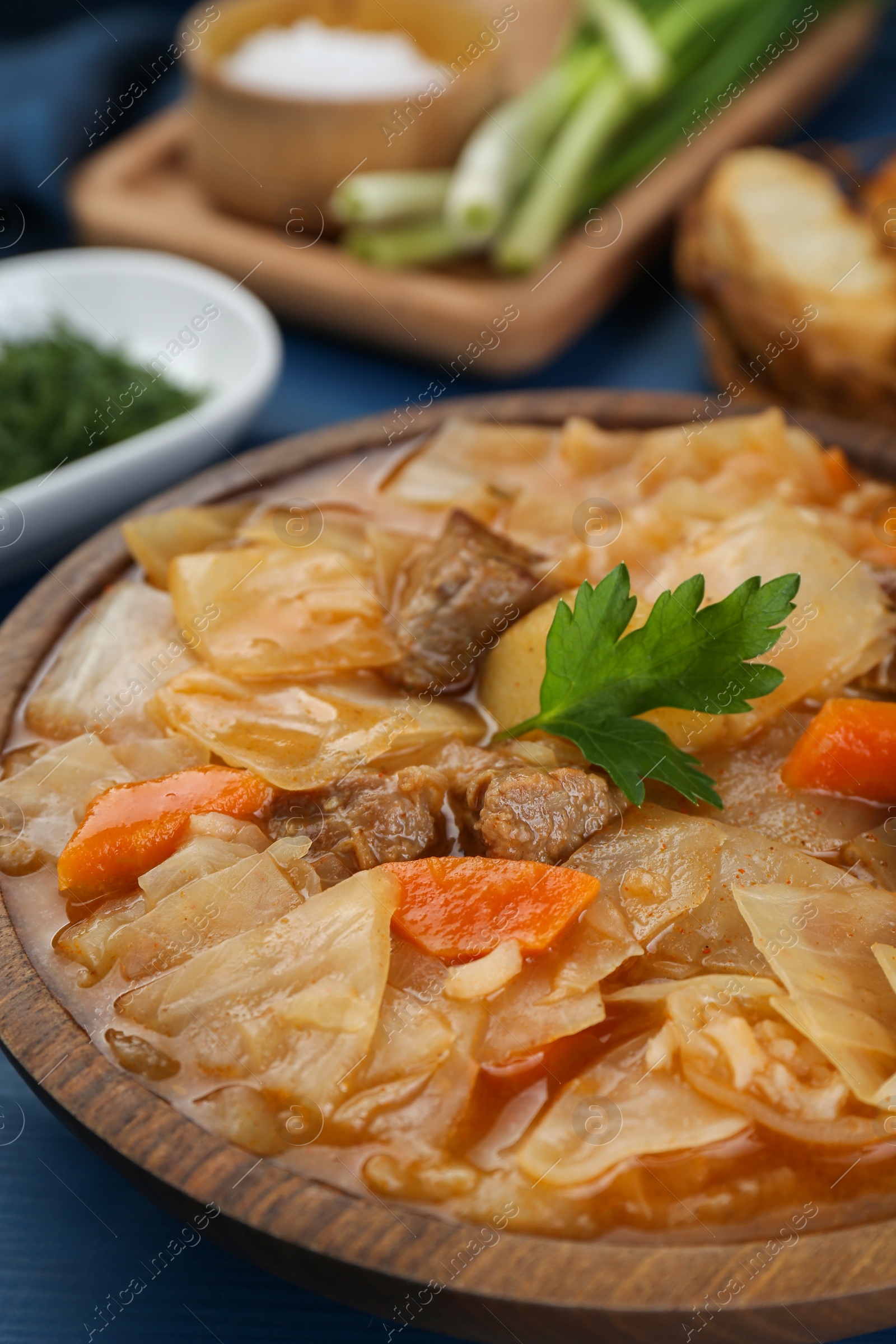 Photo of Tasty cabbage soup with meat, carrot and parsley on blue wooden table, closeup