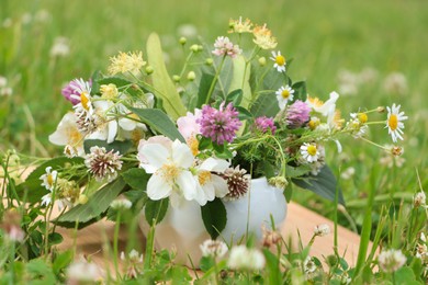 Ceramic mortar with different wildflowers and herbs on wooden board in meadow