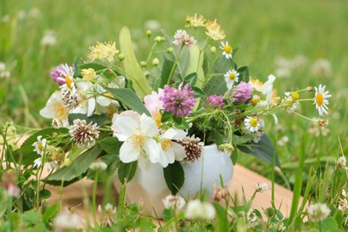 Photo of Ceramic mortar with different wildflowers and herbs on wooden board in meadow