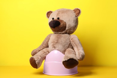 Photo of Teddy bear on pink baby potty against yellow background. Toilet training
