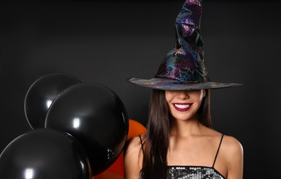 Beautiful woman wearing witch costume with balloons for Halloween party on black background