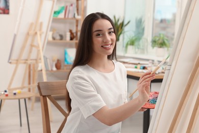 Photo of Beautiful young woman painting with brush in studio. Creative hobby