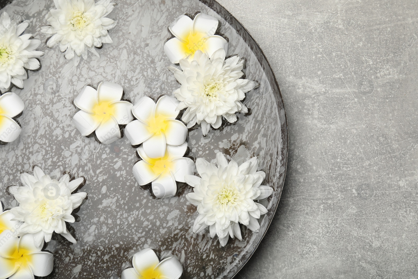 Photo of Bowl of water with flowers on light grey table, top view and space for text. Spa treatment