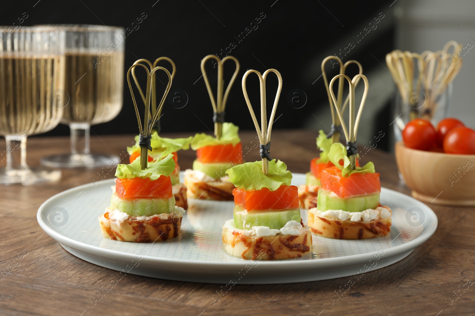 Photo of Tasty canapes with salmon, cucumber, bread and cream cheese on wooden table