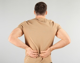 Photo of Young man suffering from back pain on light background