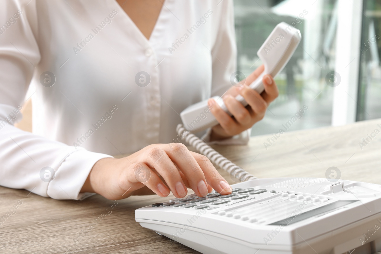 Photo of Woman dialing number on telephone at table indoors, closeup