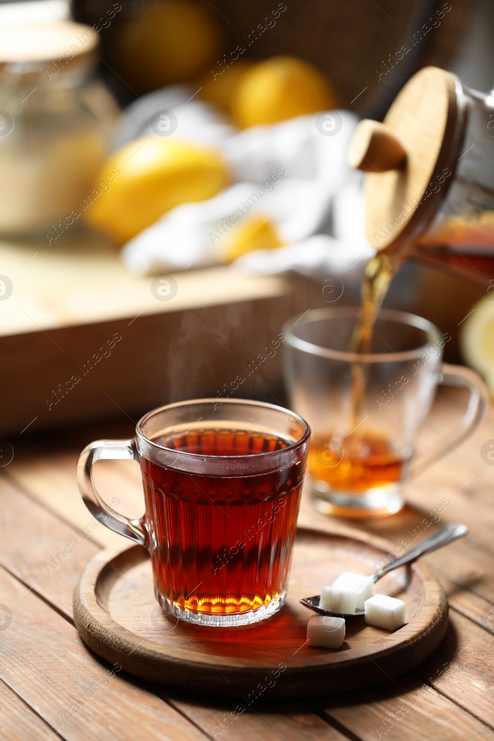 Photo of Glass cup with delicious tea and sugar on wooden table, space for text