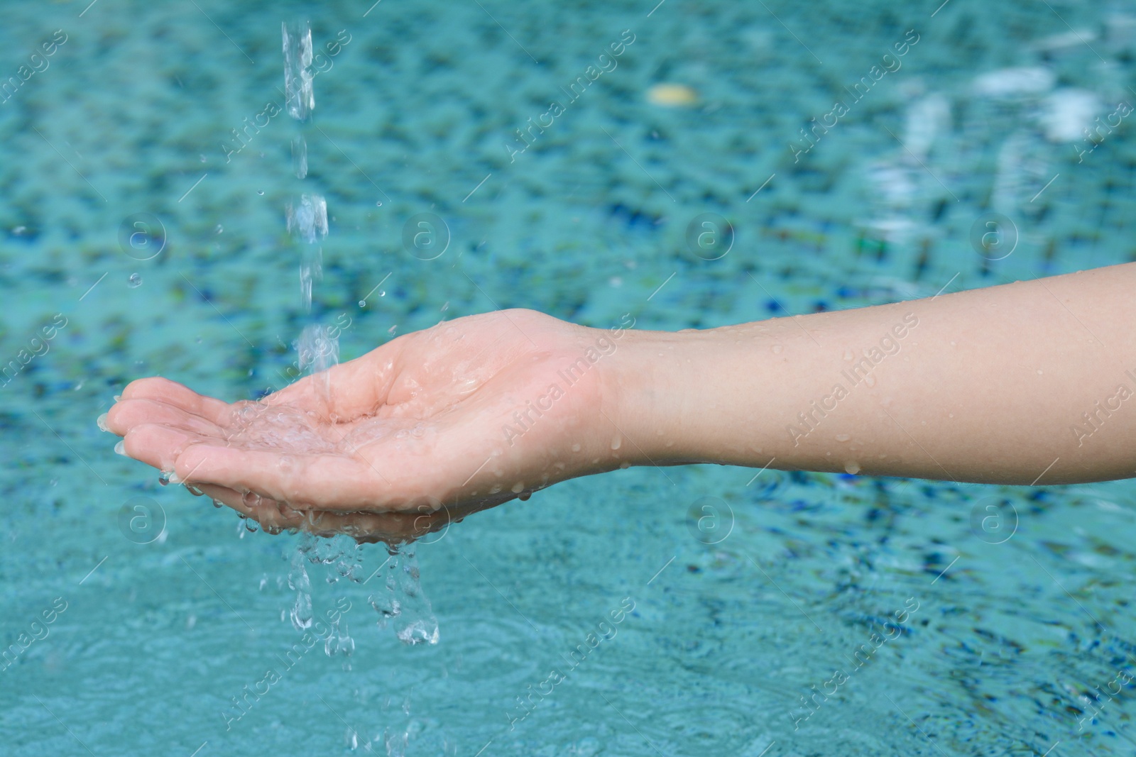 Photo of Water pouring into the girl's hand above pool, closeup